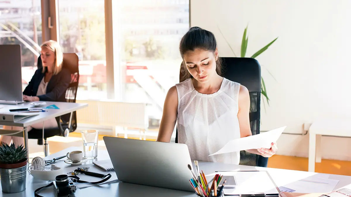 Como modernizar sistemas legados em seguradoras: Equipe de escritório trabalhando em laptops e analisando documentos em uma sala moderna, com foco em inovação e atualização de processos de TI em seguradoras