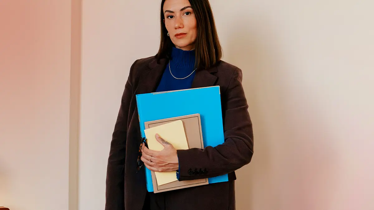 LGPD nas empresas: Profissional de escritório em ambiente corporativo, segurando pastas e documentos em mãos, com roupa social escura e tom de azul, em foto voltada a gestão e conformidade.