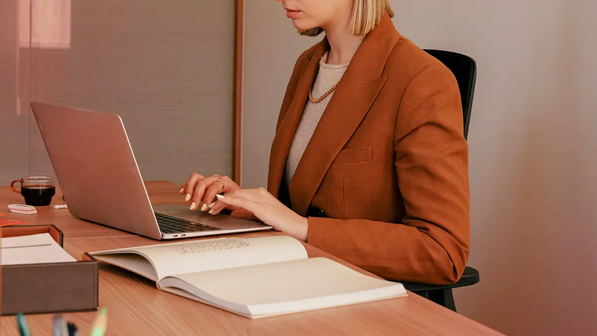 Profissional em escritório analisando documentos e usando notebook em uma mesa com planejamento financeiro, trabalhando em atendimento de seguros Core System de Seguros.