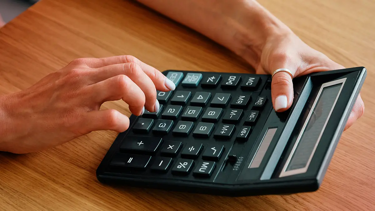 Mãos digitando em uma calculadora financeira sobre uma mesa de madeira, com foco em números e cálculos, representando Gestão de dados corporativos no dia a dia administrativo.