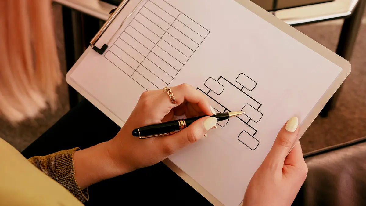 Microsserviços vs Monolito: Pessoa desenhando um diagrama com blocos e linhas em um papel, usando caneta e apontando para a estrutura, com foco em planejamento de arquitetura de software