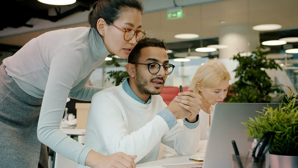 API Management para seguradoras: Equipe em escritório analisa informações em computadores: uma pessoa aponta para a tela enquanto outras consultam documentos e tomam notas, em ambiente corporativo moderno.