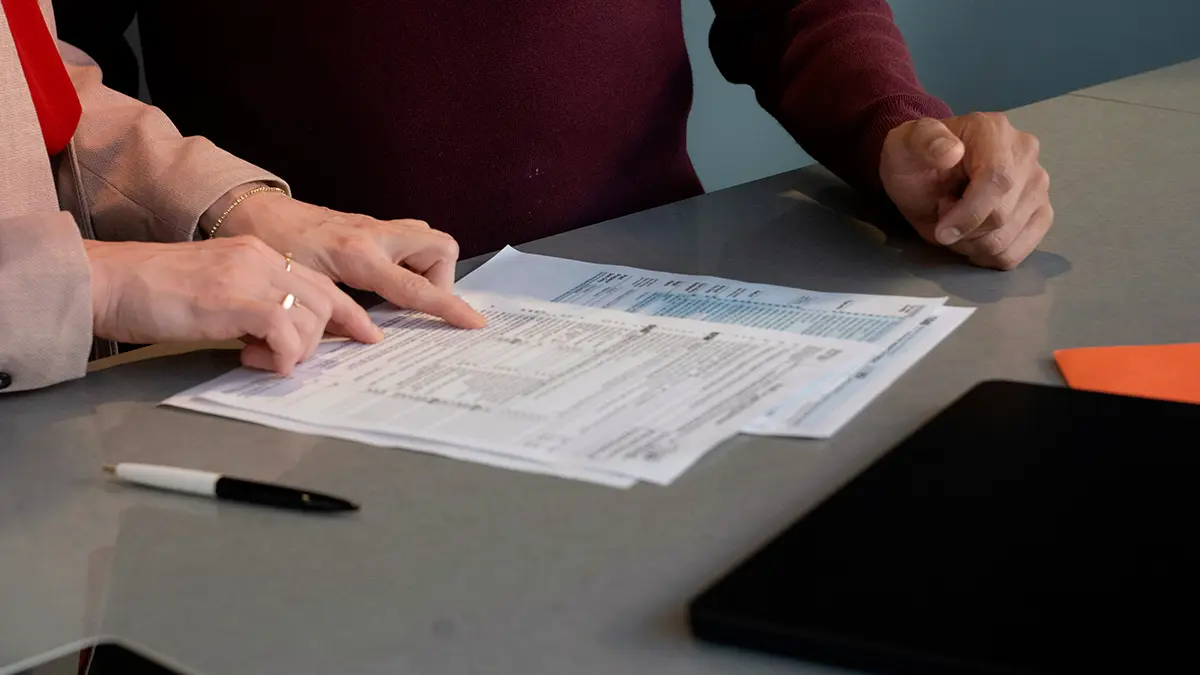 Equipe analisando documentos em uma mesa durante um processo de trabalho, com formulários e mãos assinando papéis, cenário que remete a automação de sinistros.
