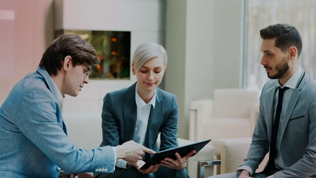 Equipe em ambiente corporativo analisando uma tela de tablet, com um profissional usando tablet e outros dois em volta, discutindo dados enquanto planejam soluções — inteligência artificial em seguros