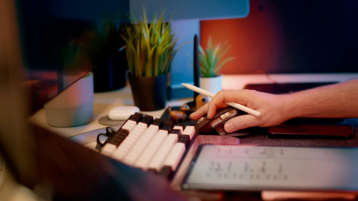 observabilidade em sistemas de seguros: Mão segurando caneta em frente a um teclado e a um documento aberto na área de trabalho, com tela de computador ao fundo e ambiente de escritório durante tarefas administrativas.