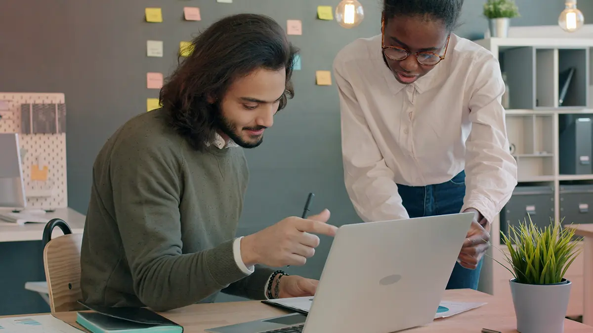 Dois profissionais em um escritório analisam documentos em um laptop e em um tablet, discutindo com seriedade enquanto anotam; a cena sugere uso de tecnologia para automação. Agentes de IA para seguradoras