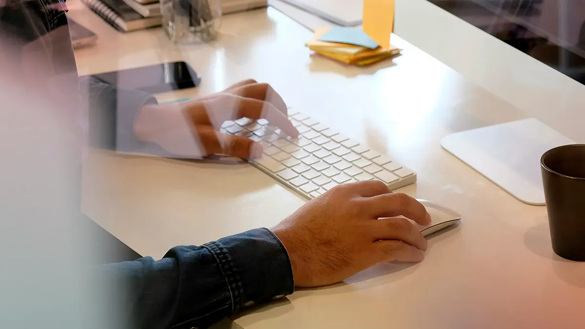 IA na subscrição de seguros: Pessoa usando teclado de computador enquanto trabalha em uma mesa de escritório com documentos e caneta ao lado, em ambiente corporativo, sugerindo automação e tecnologia para processos de seguros.