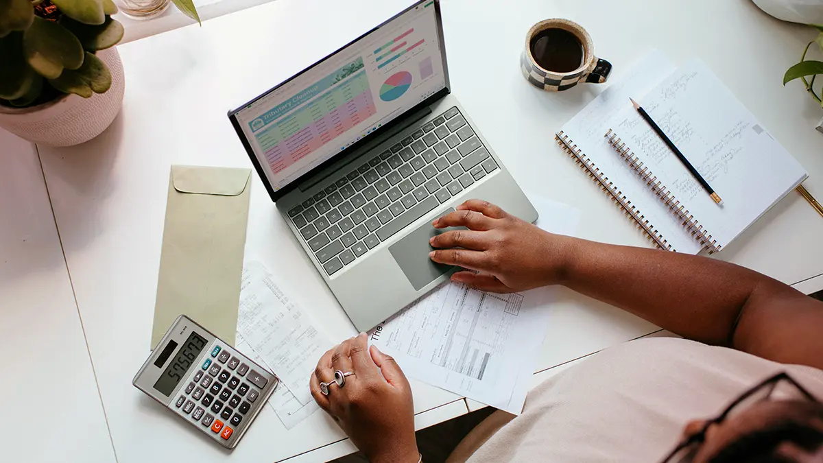 reforma tributária no setor de seguros: Mesa de trabalho com pessoa analisando documentos e gráficos em notebook, calculadora e calculando números financeiros para projetos e planejamento, com caneta e caderno abertos.