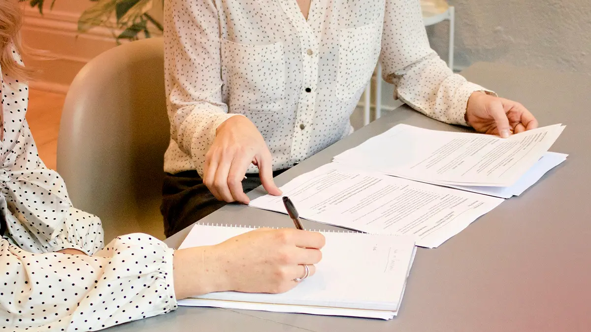 Pessoa assinando documentos em mesa com caneta, em ambiente de escritório, com papéis e formulários sobre a mesa, relacionado a sistema de resseguro e acordos financeiros